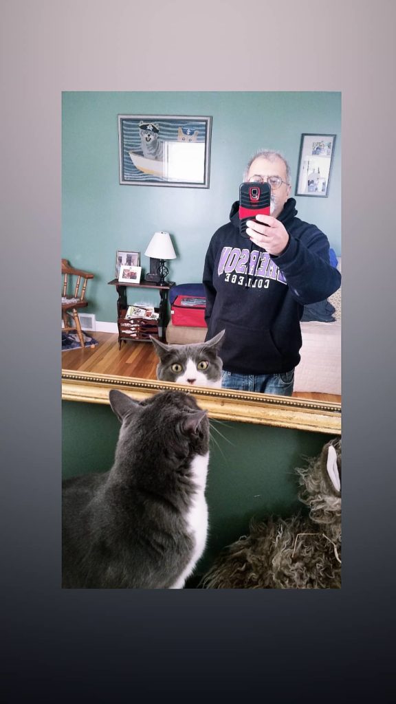 Carson the cat sees himself in the mirror with me behind capturing the moment with my cellphone.